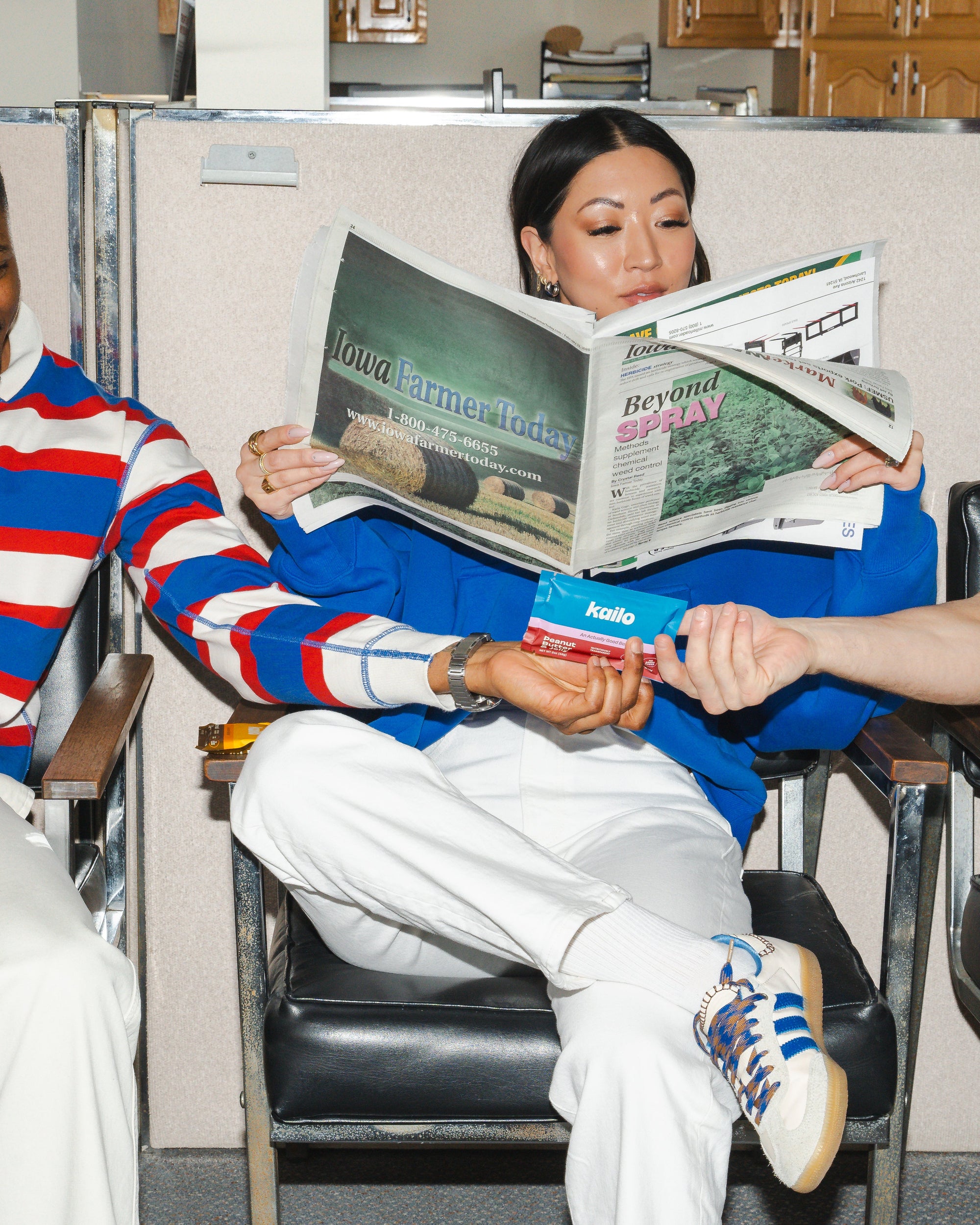 Three people sitting together, one reading a magazine, in an office setting.