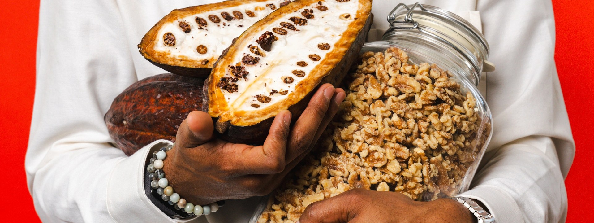 Raw cacao pods and a jar of walnuts held in both arms