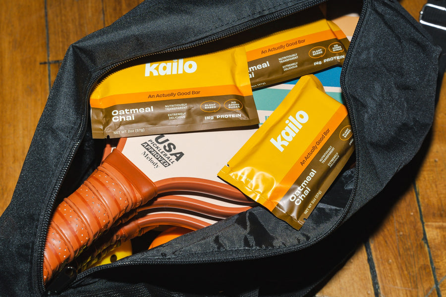 Two Oatmeal Chai Kailo bars tucked into a pickleball bag beside paddles