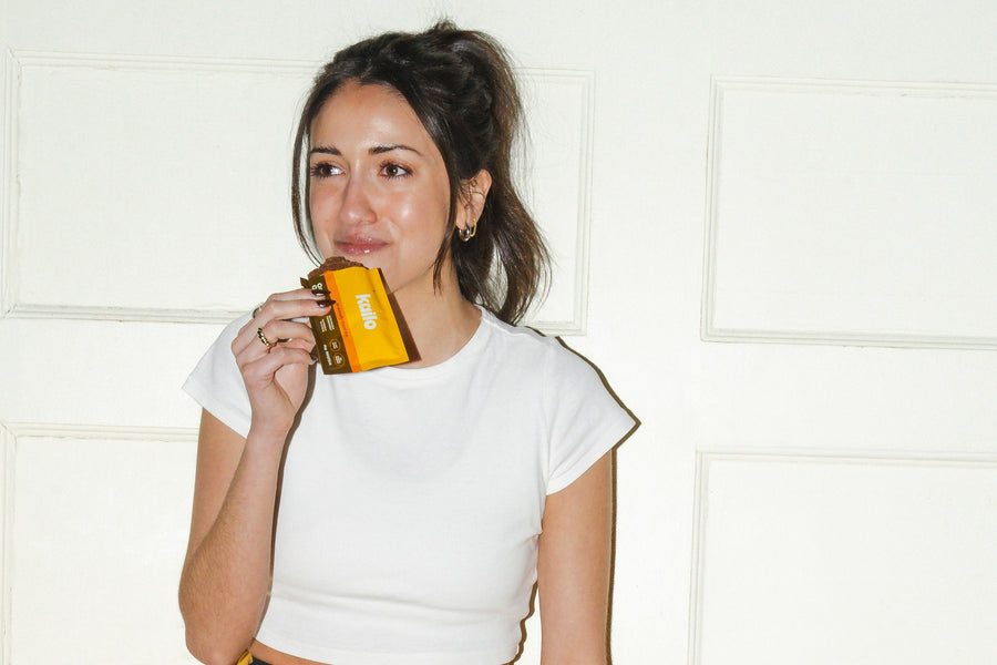 A woman in workout clothes taking a bite of a Kailo Oatmeal Chai bar